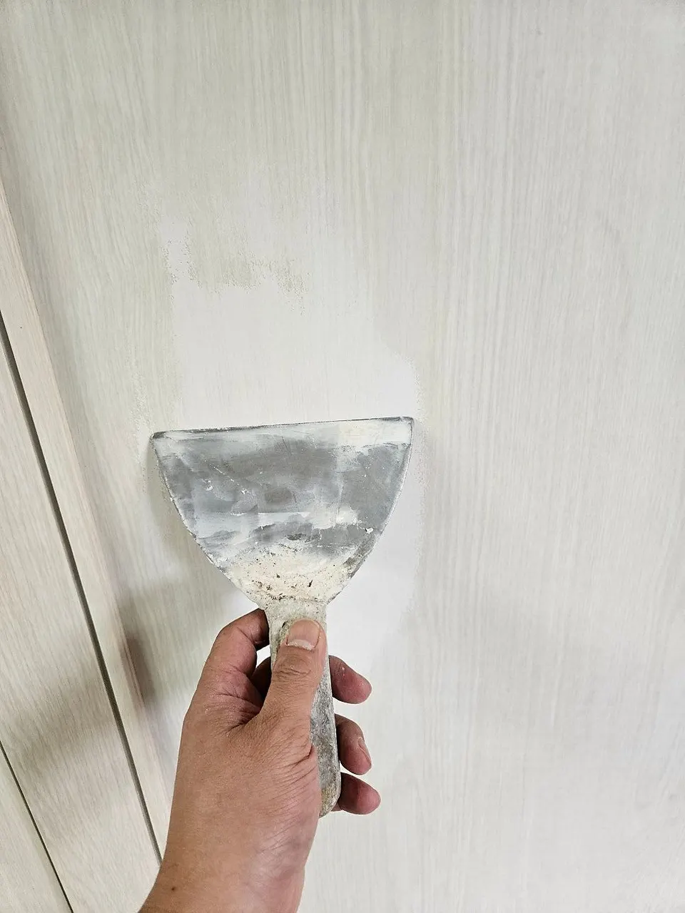 주걱으로 문 표면에 퍼티를 펴 바르는 모습