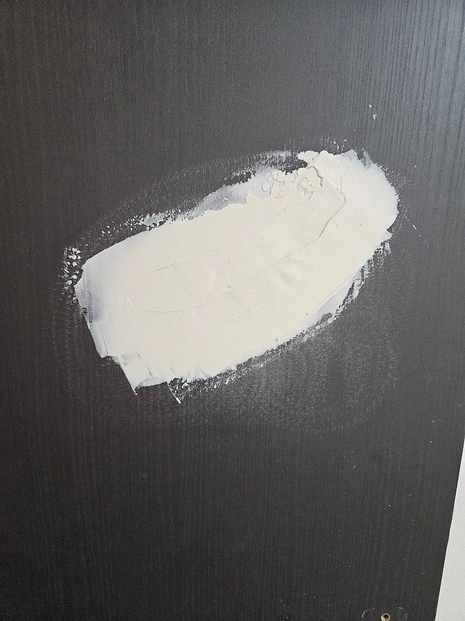 구멍 자리를 퍼티로 메워 하얗게 면을 잡은 문 표면
